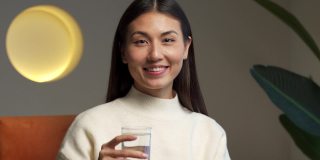 一个快乐美丽的年轻亚洲妇女，手里拿着一杯干净的水，看着相机。一个快乐微笑的年轻女子的肖像，一杯新鲜的水