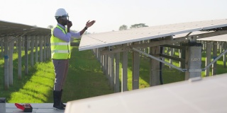 在太阳能发电厂安装太阳能电池板的过程中，身穿防护服、带反光布的非洲青年工程师攀爬并站在结构上，通过无线电侧视图与团队沟通