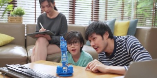 在家学习的概念，亚洲男孩的孩子与父亲和母亲成功控制机器人手臂上的数字平板电脑和电脑键盘，快乐的家庭得到了一课编码控制机器人在家里
