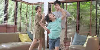 幸福快乐的亚洲家庭，爸爸妈妈和儿子滑稽的舞蹈在客厅在家里。有趣的时刻，在家跳舞，一起享受节日。亚洲家庭共度美好时光的概念。