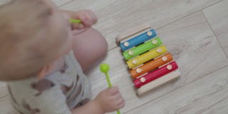 可爱的小男孩坐在地板上玩着五颜六色的木琴音乐玩具，10个月大的小男孩待在家里。乐器供孩子们学习演奏音乐。