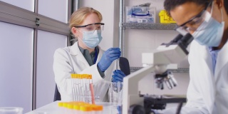 穿戴个人防护装备的实验室女工作人员在实验室用显微镜分析样品
