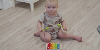可爱的小男孩坐在地板上玩着五颜六色的木琴音乐玩具，10个月大的小男孩待在家里。乐器供孩子们学习演奏音乐。