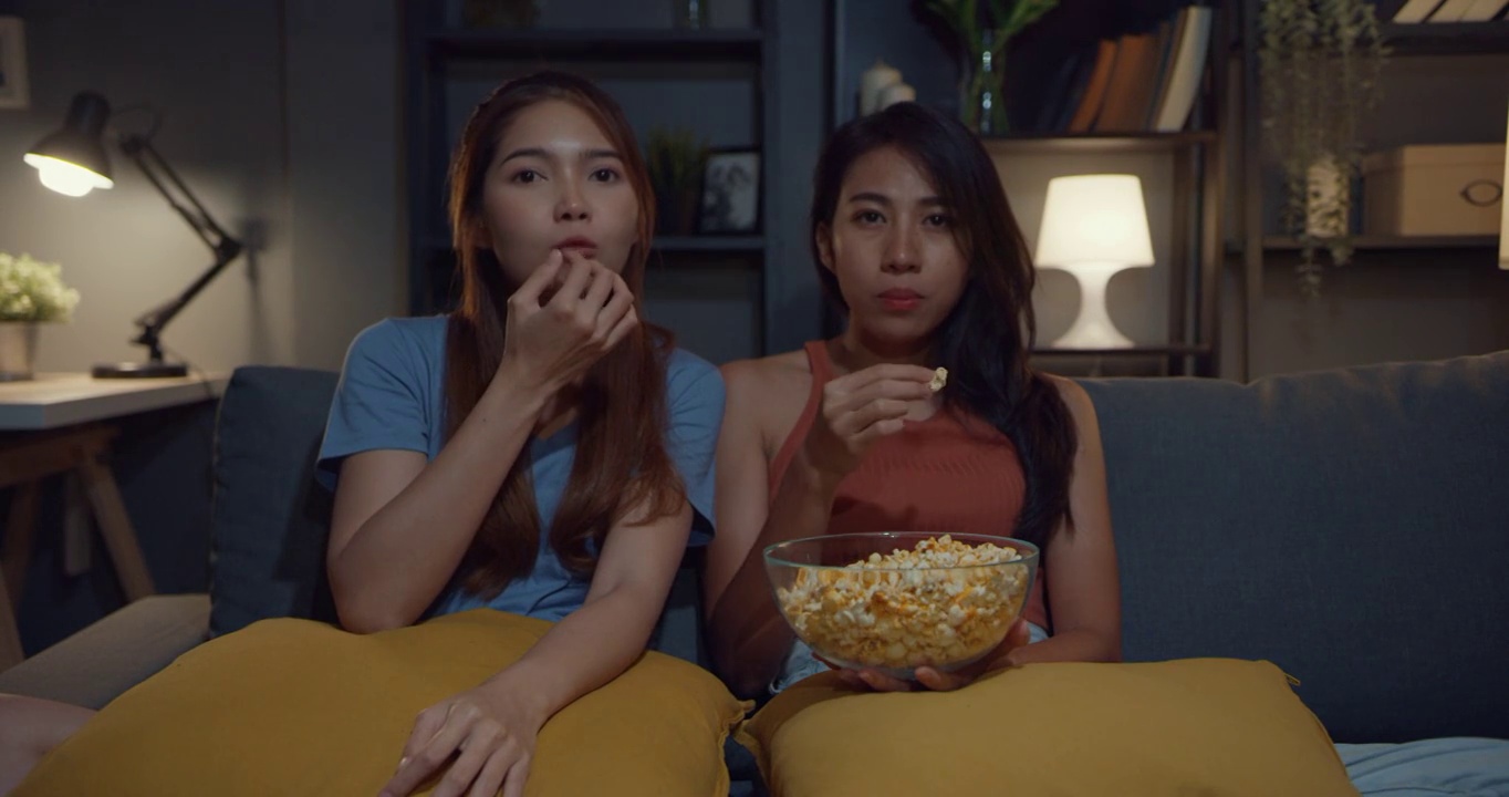 有吸引力的亚洲夫妇女士休闲享受快乐的时刻，焦点看在线电影娱乐吃爆米花网站在家里的沙发客厅晚上。生活方式活动隔离概念。