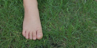 夏天的时候，小娃娃踩在绿色的草地上。赤足儿童特写视图