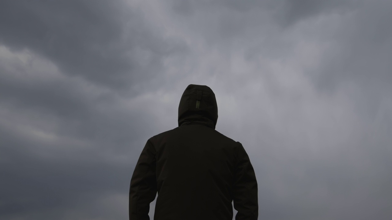 男性穿着连帽夹克的背影在天空中黑色的忧郁戏剧性的云
