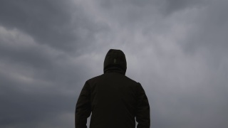 男性穿着连帽夹克的背影在天空中黑色的忧郁戏剧性的云视频素材模板下载