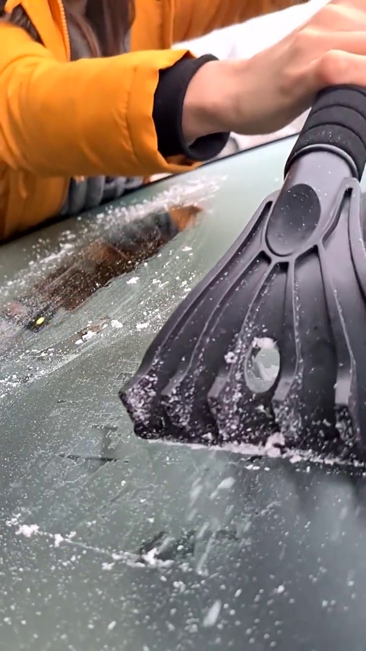 一名妇女正在努力清除车窗上的冰块。早上在宽屏上与冰的斗争。
