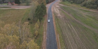 白色电动汽车在乡村道路上的鸟瞰图。现代汽车通过农村公路。
