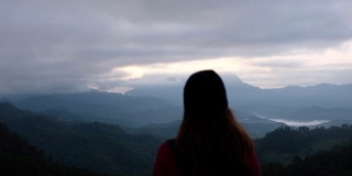 一个女性旅行者的后视图，看着一个美丽的山景在雾天