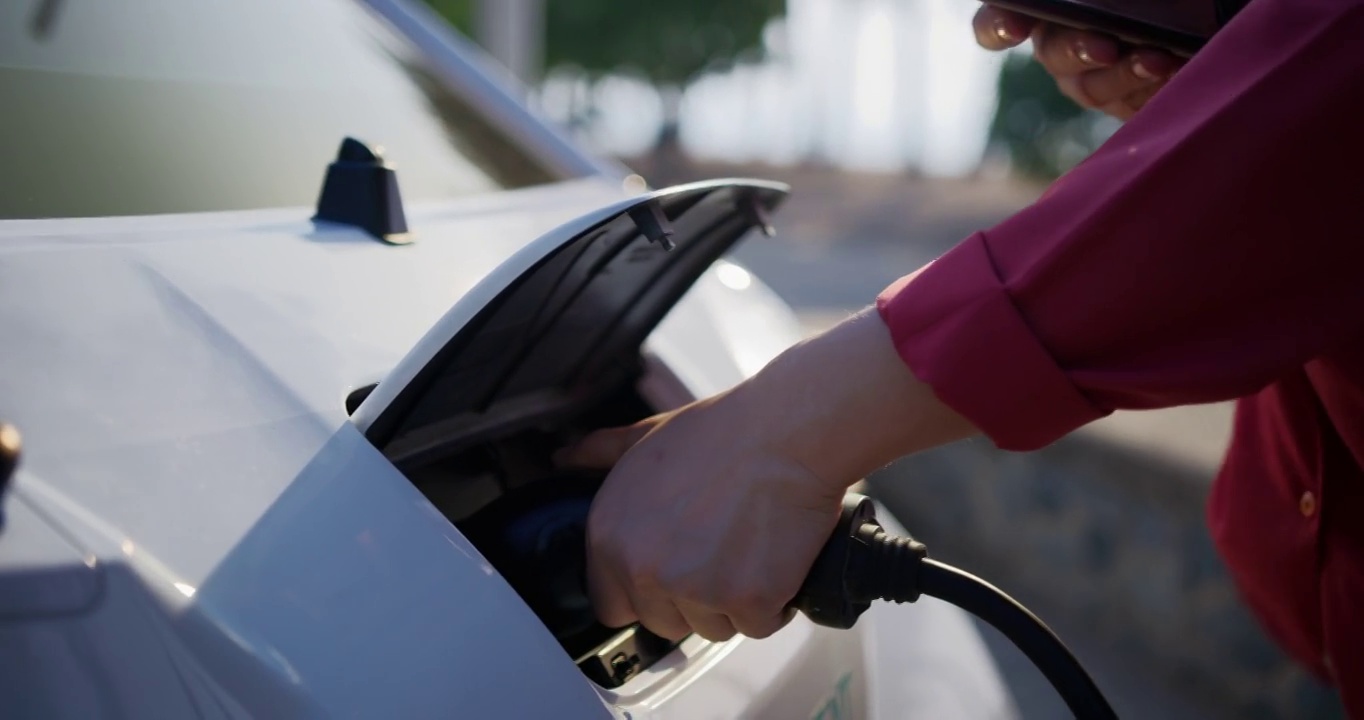 一名女子给电动汽车充电，并使用智能手机检查电池状态