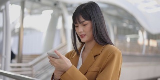 成功的女雇员的肖像。美丽，亚洲年轻女子快乐的微笑使用智能手机站在时尚的城市。商业人，技术观念。可以在任何地方工作，上网。