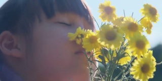 在一个阳光明媚的夏日，一个可爱的小女孩正在闻她手里捧着的一束花。快乐的孩子享受大自然的户外。从花香中体味感官学习。