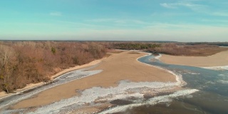 无人机拍摄的画面显示，冬天的时候，在有一条小河的沙滩上飞行