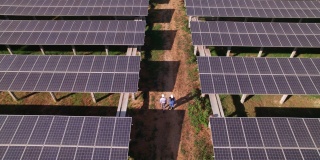 工程师和技术员在太阳能电池板的阴影下检查太阳能电池板农场，电力，太阳能产生的清洁能源的鸟瞰图