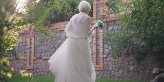 欢快美丽的高级新娘在阳光下旋转跳舞在户外慢动作。广角镜头激动自信的白人退休人员喜结大喜。幸福与活力理念。