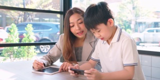 一个男孩在咖啡厅里用智能手机玩游戏，旁边站着一位女商人。女人和孩子说话。幸福和微笑。社交媒体。网络技术。教育、学习和娱乐