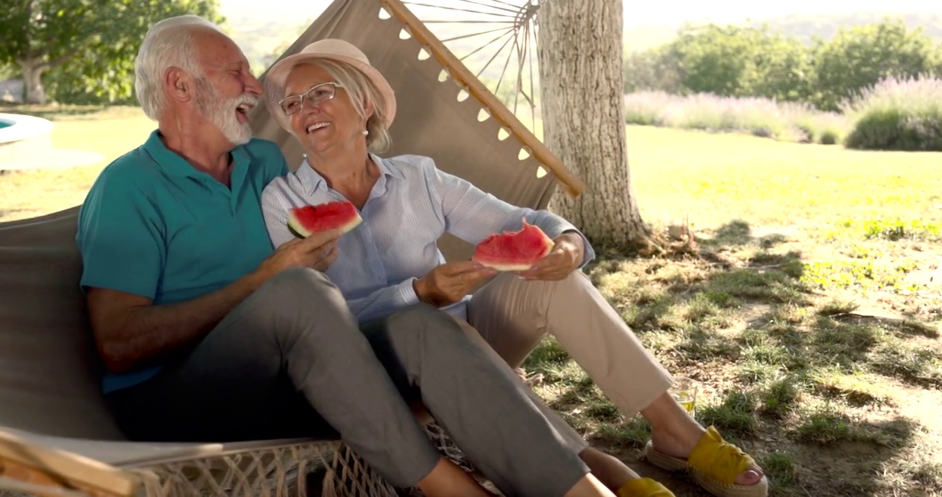 快乐的老夫妻在吊床上边吃西瓜边聊天。