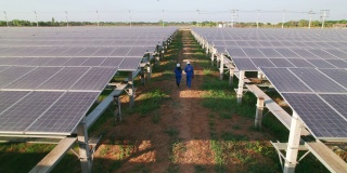 鸟瞰图，男男女女蓝领工人在检查大型太阳能农场、电力、太阳能产生的清洁能源后，走在太阳能电池板之间的小线上