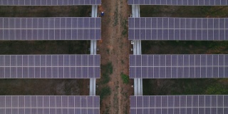 对称太阳能电池板农场的鸟瞰图，生产清洁电力的蓝领工人在中间的小轨道
