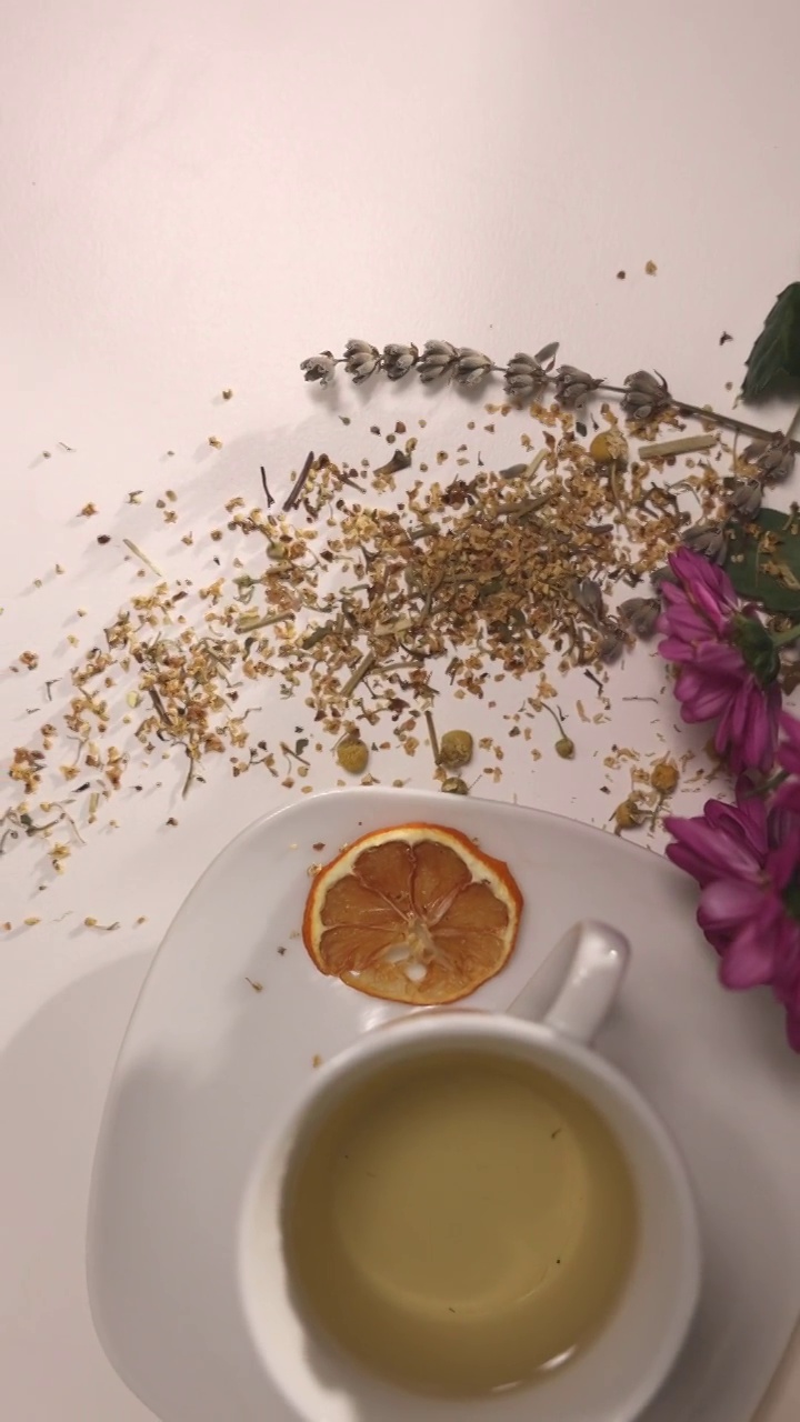高角度的陶瓷茶杯在桌子上，桌子上有草药，蜂蜜罐，鲜花