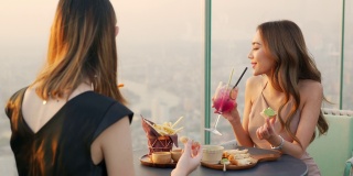 4K亚洲女性朋友在夏日夕阳下在摩天大楼的屋顶餐厅共进晚餐。