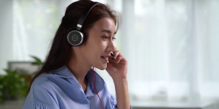 在工作中感到快乐和积极。年轻的亚洲女商人戴着耳机在笔记本电脑上与客户进行视频通话。年轻的亚洲女性提供在线教育课程讲座，咨询客户。