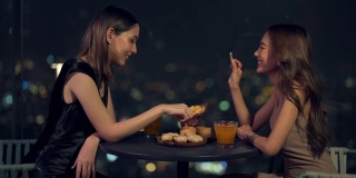 晚上，4K亚洲女性朋友在摩天大楼的屋顶餐厅吃晚餐，喝鸡尾酒。