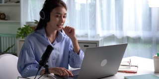 在工作中感到快乐和积极。年轻的亚洲女商人戴着耳机在笔记本电脑上与客户进行视频通话。年轻的亚洲女性提供在线教育课程讲座，咨询客户。