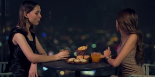 晚上，4K亚洲女性朋友在摩天大楼的屋顶餐厅吃晚餐，喝鸡尾酒。