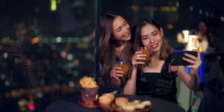 4K亚洲女性朋友晚上在屋顶餐厅吃饭时一起用智能手机自拍。