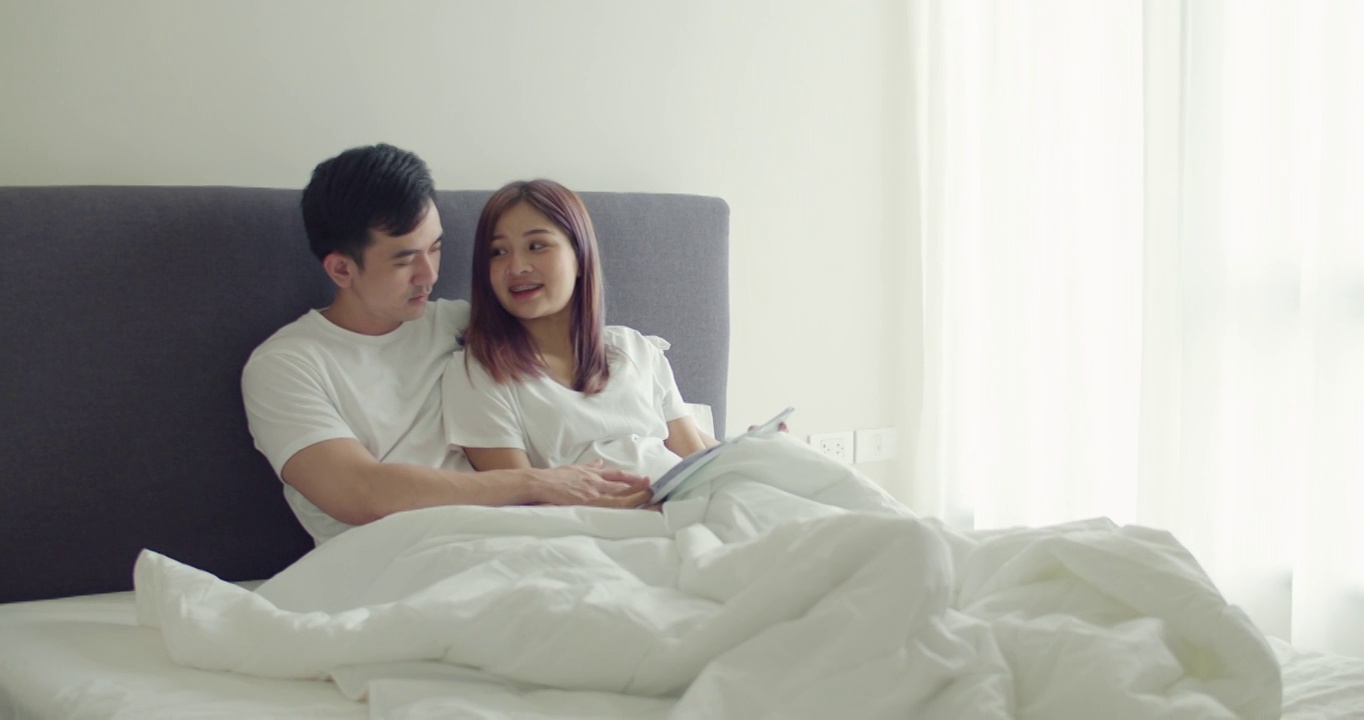 亚洲丈夫和怀孕的妻子会在卧室里一起读书给孩子听。