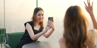 日落时分，4K亚洲女性朋友在屋顶餐厅用智能手机拍照。