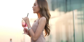 日落时分，一名4K亚洲女子在摩天大楼的屋顶餐厅喝着鸡尾酒等朋友。