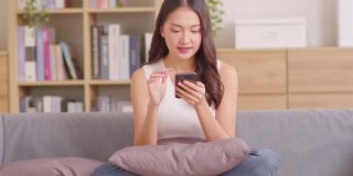 千禧一代的亚洲年轻女性看着手机笑着说着好消息或在家网上购物的折扣券。快乐而开朗的女人看着手机app读着短信感到兴奋
