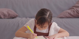 肖像小亚洲女孩学习学习在家里微笑和幸福。可爱的女孩在笔记本上画画和写字，以提高自己的技能和情商。家庭学校教育理念