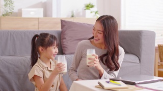 亚洲母亲和她的女儿碰杯享受和微笑的牛奶饮料。妈妈和小女孩拿着牛奶杯喝来补充钙质。健康饮食的概念视频素材模板下载