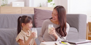 亚洲母亲和她的女儿碰杯享受和微笑的牛奶饮料。妈妈和小女孩拿着牛奶杯喝来补充钙质。健康饮食的概念