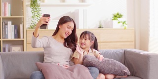 年轻的亚洲妈妈和她的女儿视频电话会议与家人一起玩。幸福妈妈和小女孩一边看着手机一边挥着手和外婆视频聊天