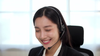 呼叫中心smiley亚洲商务女接待员戴耳机视频会议电话，在电脑上通过网络摄像头在网上聊天，客户支持服务。视频素材模板下载
