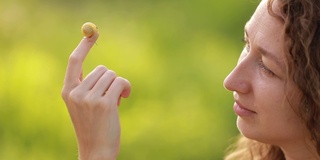 女人抱着蜗牛的特写在绿色的自然背景上。蜗牛坐在手上或手掌上，慢慢地爬过年轻女孩的皮肤。欣赏野生动物或自然的女性。蜗牛美容精华。