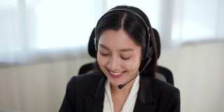 Smiley亚洲商务女接待员戴耳机视频会议电话，在电脑上通过网络摄像头在网上聊天，客户支持服务。