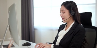 呼叫中心smiley亚洲商务女接待员戴耳机视频会议电话，在电脑上通过网络摄像头在网上聊天，客户支持服务。