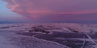 冻结的湖的北方景观无人机飞行下来与美丽的倒影在冰在日落。令人惊叹的冬季贝加尔湖，红色的日出。看一架无人机在北部冰湖上飞行。自然反射日落