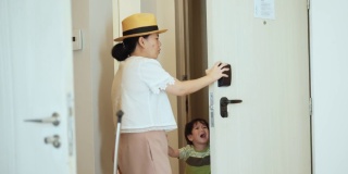 带着孩子的亚洲妇女穿过酒店走廊，用钥匙卡开门，带着行李进入房间。周末度假:当地自驾游。