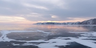 北方景观冻结湖无人机飞行下来与美丽的反射在日落4K。令人惊叹的冬季贝加尔湖和红色的日出。观看无人机在北方霜冻湖上的飞行。自然反射日落