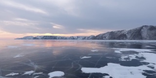 北方景观冻结湖无人机飞行下来与美丽的反射在日落4K。令人惊叹的冬季贝加尔湖和红色的日出。观看无人机在北方霜冻湖上的飞行。自然反射日落