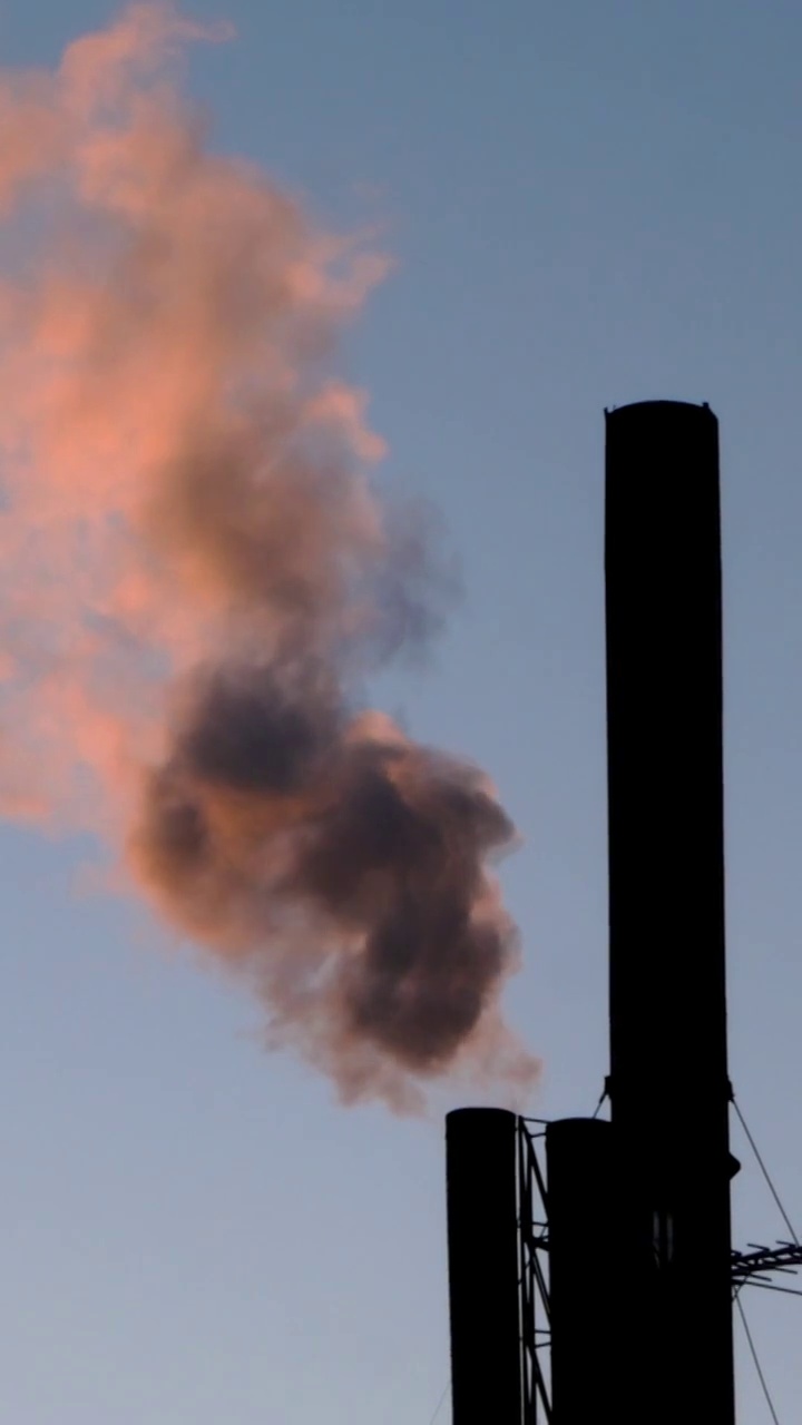夕阳下，从工业烟囱、锅炉房或工厂冒出的红色烟雾。能源生产和污染环境的工业生产。