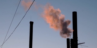 夕阳下，从工业烟囱、锅炉房或工厂冒出的红色烟雾。能源生产和污染环境的工业生产。