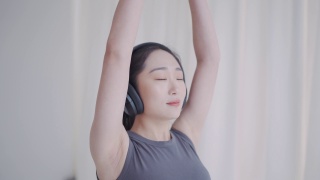 年轻的亚洲女性用无线耳机练习瑜伽冥想视频素材模板下载